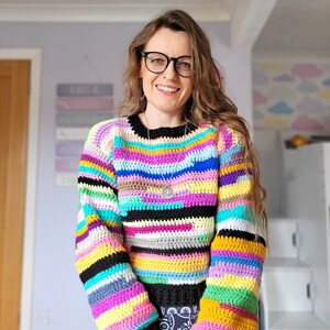 May include: A colorful striped crochet sweater with long sleeves. The sweater is made with a variety of colors, including black, white, pink, yellow, blue, green, and purple.