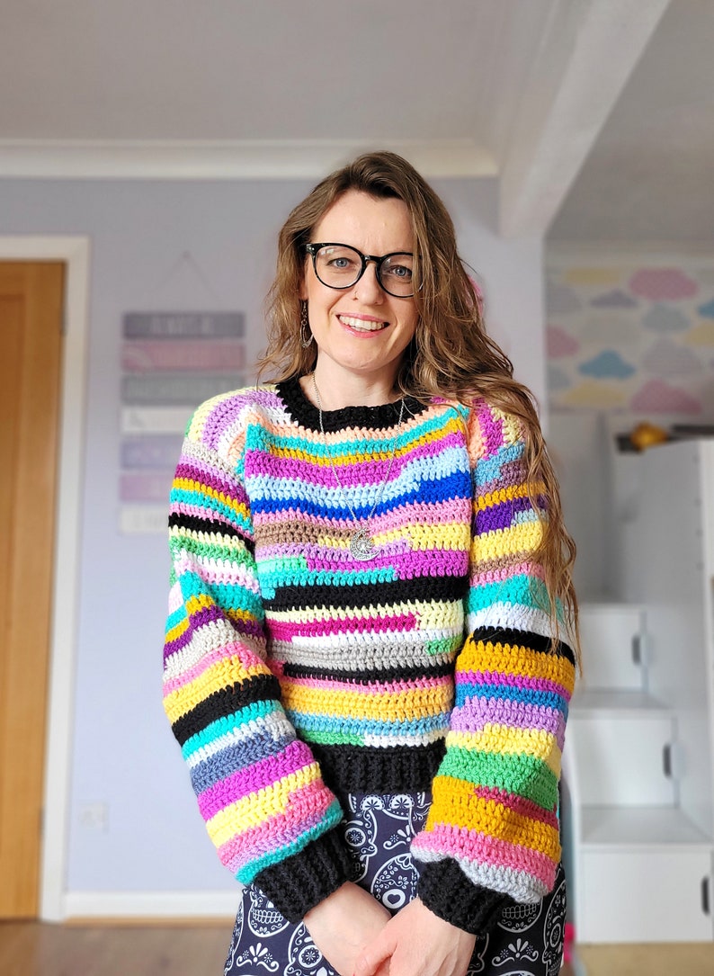 May include: A colorful striped crochet sweater with long sleeves. The sweater is made with a variety of colors, including black, white, pink, yellow, blue, green, and purple.