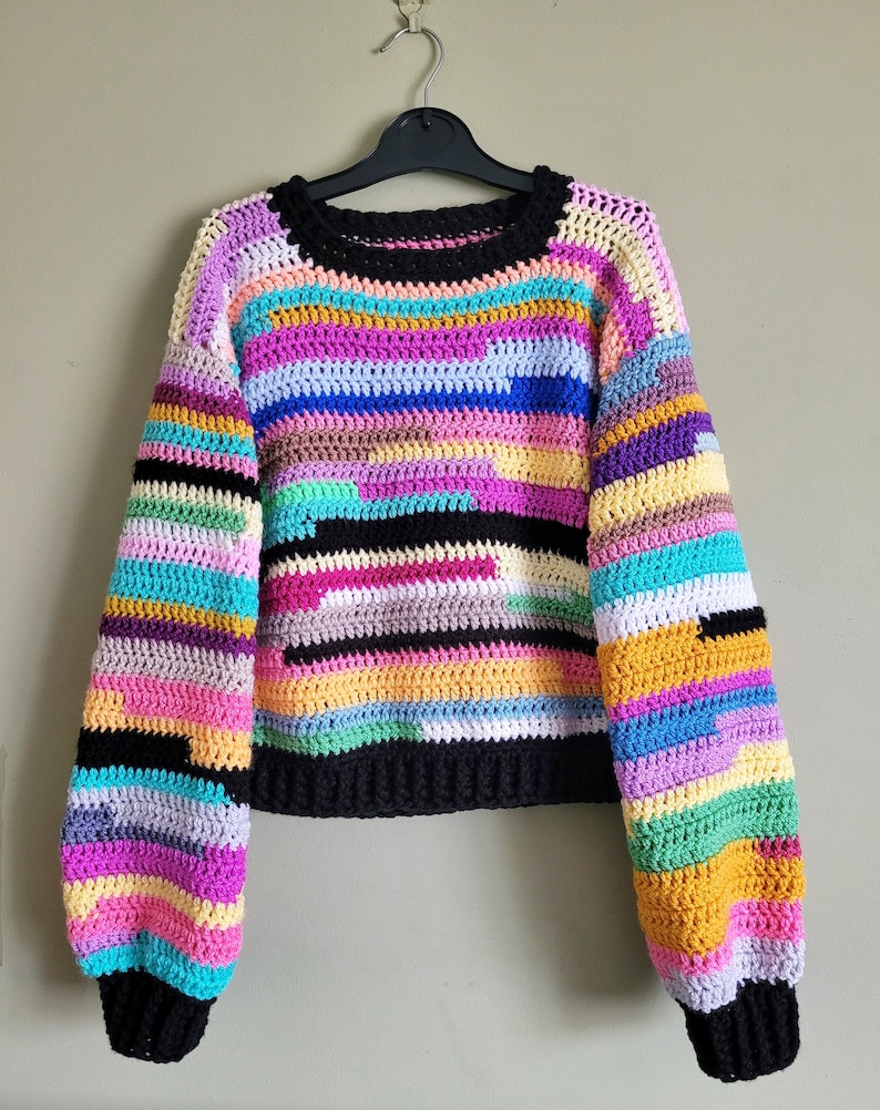 May include: A colorful striped crochet sweater with long sleeves and a round neckline. The sweater is made with a variety of bright colors, including pink, blue, green, yellow, and orange.
