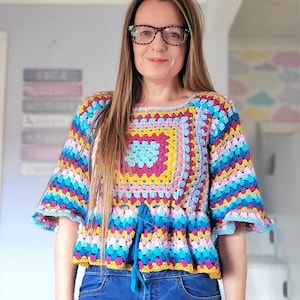 May include: A colorful crocheted top with a square design in the center and a tie at the waist. The top is worn with blue jeans.