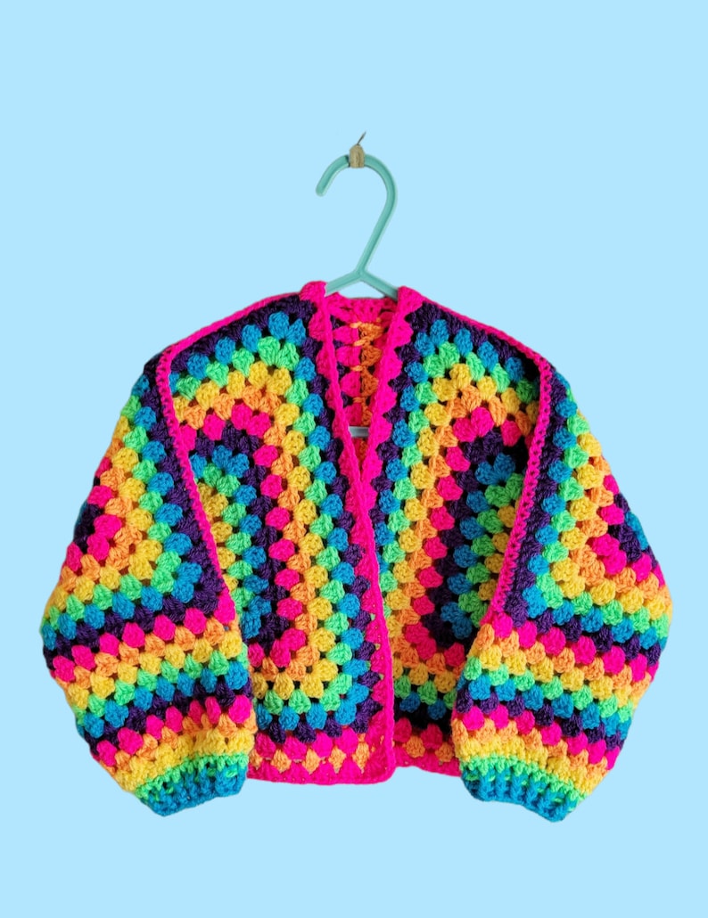 May include: A rainbow crochet cardigan with a granny square pattern. The cardigan has long sleeves and a V-neck.