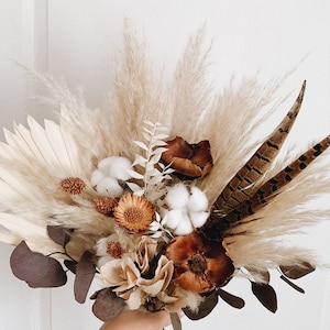 May include: A dried flower bouquet with pampas grass, cotton bolls, pheasant feathers, and dried eucalyptus leaves in shades of brown, beige, and white.
