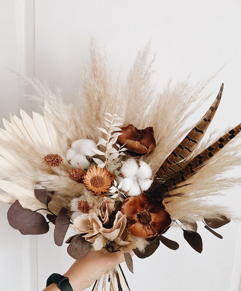 May include: A dried flower bouquet with pampas grass, cotton bolls, pheasant feathers, and dried eucalyptus leaves in shades of brown, beige, and white.