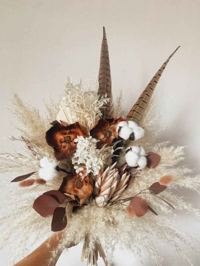 May include: A dried flower bouquet with white pampas grass, brown feathers, dried eucalyptus leaves, and cotton bolls.