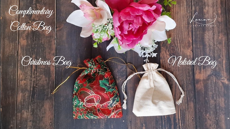 May include: Three drawstring bags on a wooden surface. The bags are made of different materials: a red and green Christmas-themed bag, a plain white cotton bag, and a natural-colored cotton bag.