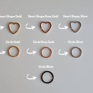 May include: A set of six key rings in different shapes and colors. The key rings are in the shape of a heart and a circle. The colors are gold, rose gold, silver, and black.