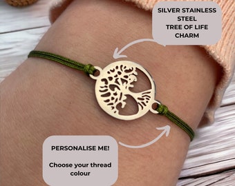 May include: A green string bracelet with a silver stainless steel tree of life charm. The charm is round and features a detailed tree design. The text "PERSONALISE ME! Choose your thread colour" is visible in the image.