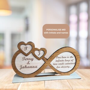 Puede incluir: S&iacute;mbolo de infinito de madera con dos corazones, personalizado con los nombres "Terry & Johanna" y las iniciales "T" y "J". El s&iacute;mbolo de infinito tiene el texto "Nuestro amor es el bucle infinito de dos almas entrelazadas por la eternidad..."