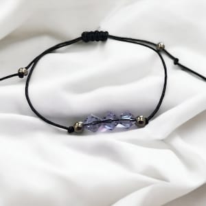 May include: A simple adjustable bracelet with a black cord and silver beads. The bracelet features a row of four purple crystal beads.