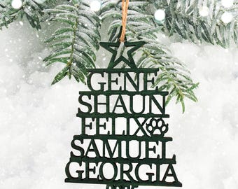 Puede incluir: Adorno de árbol de Navidad verde oscuro con los nombres "GENE", "SHAUN", "FELIX", "SAMUEL" y "GEORGIA" recortados. El adorno también incluye una huella de pata y el año "2025". Cuelga de una cuerda de hilo natural.