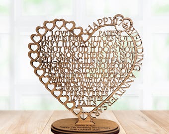 Puede incluir: Decoración de aniversario en forma de corazón de madera. El corazón está intrincadamente cortado con un borde de encaje y lleno con las palabras "El amor es paciente, el amor nunca falla". La base dice "Feliz 7º Aniversario de Bodas" y una fecha.