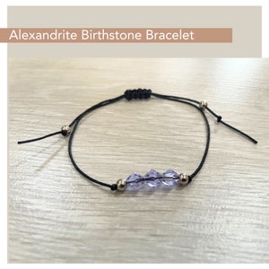 May include: A black adjustable string bracelet with a silver clasp and three purple faceted beads. Alexandrite Birthstone Bracelet.