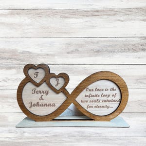 Puede incluir: S&iacute;mbolo de infinito de madera con dos corazones, grabado con los nombres "Terry & Johanna" y la cita "Nuestro amor es el bucle infinito de dos almas entrelazadas por la eternidad..."