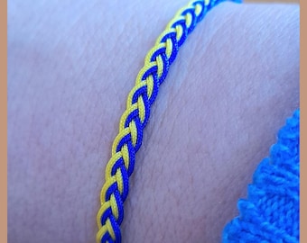 May include: A blue and yellow braided friendship bracelet. The bracelet is made of two strands of cord, one blue and one yellow, that are woven together.