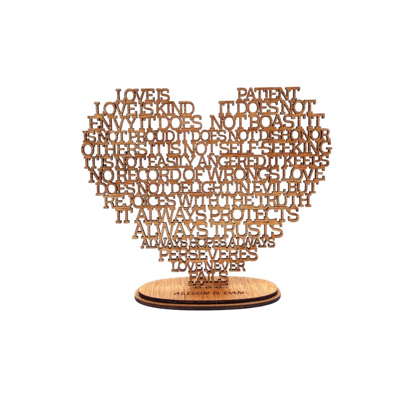 May include: A wooden heart-shaped decorative piece with the words "Love is Kind" and other phrases laser-cut into the wood. The heart sits on a round wooden base. The names "Allison & Dan" are engraved on the base.