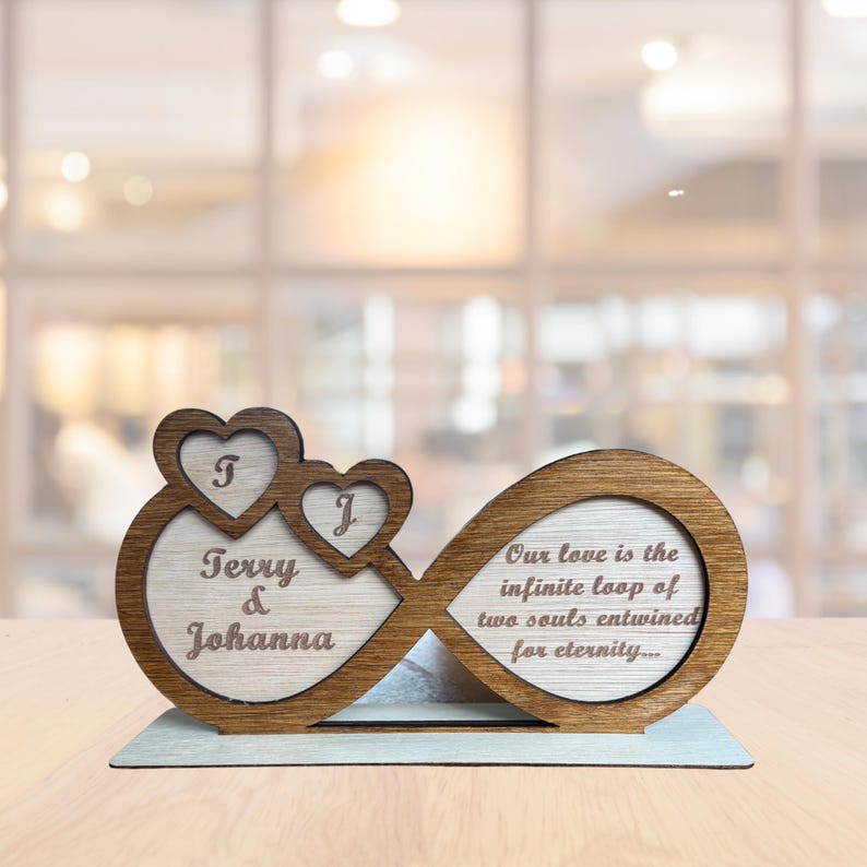Puede incluir: S&iacute;mbolo de infinito de madera con dos corazones en la parte superior, grabado con los nombres "Terry & Johanna" y la cita "Nuestro amor es el bucle infinito de dos almas entrelazadas por la eternidad..."