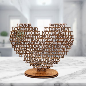 May include: A heart-shaped wooden cutout featuring laser-cut text that reads: Love is patient, love is kind. It does not envy, it does not boast, it is not proud. It does not dishonour others, it is not self-seeking. The base is engraved with Alison & Dan.