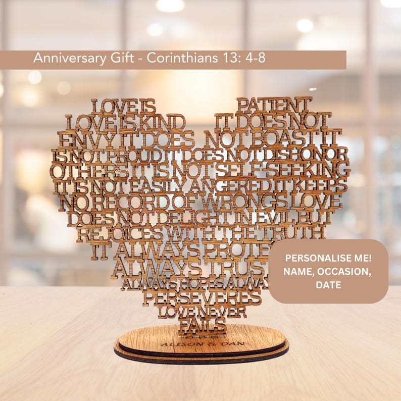 May include: Wooden heart-shaped anniversary gift with the text from Corinthians 13:4-8. The words are laser-cut and arranged to form the heart. The base is a round wooden stand. The text "Personalise me!" is also visible.