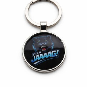 May include: Round keychain with a black background featuring a snarling panther graphic with blue and white accents. The text "IT'S JAAAAAG!" is in blue and white. The keychain has a silver-colored metal ring.