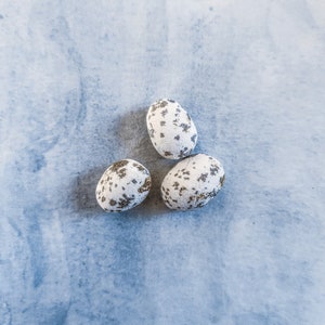 May include: Three speckled white eggs against a grey background.