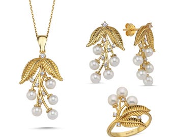 May include: A gold-tone jewelry set featuring a pendant necklace, earrings, and a ring. Each piece features a delicate design of leaves and pearls.