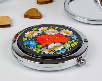May include: A set of small, round, silver-framed mirrors with colourful floral designs painted on the front. The mirrors are closed and open, showing the reflective surface inside.
