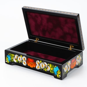 May include: Black wooden box with a red velvet interior and a floral design painted on the exterior. The flowers are white, red, yellow, blue, and green.
