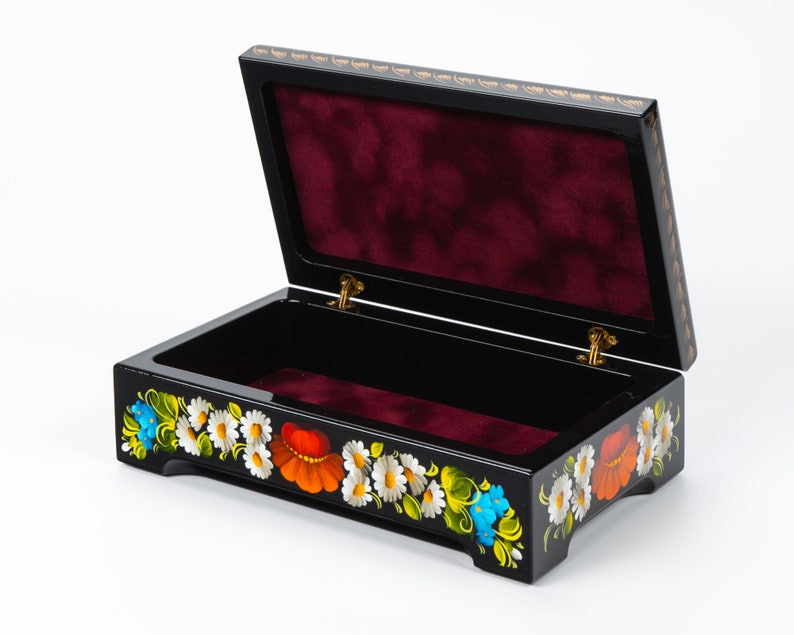 May include: Black wooden box with a red velvet interior and a floral design painted on the exterior. The flowers are white, red, yellow, blue, and green.