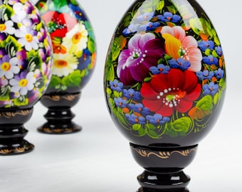 Op de afbeelding: Drie zwarte houten eieren met handgeschilderde bloemenmotieven. De eieren staan op zwarte standaards en hebben een glanzende afwerking.