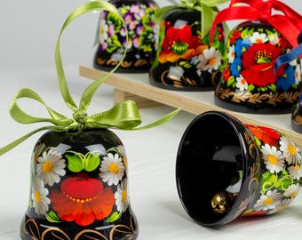 Puede incluir: Un conjunto de seis campanas pintadas de negro con diseños florales coloridos. Las campanas están decoradas con flores rojas, blancas, azules, verdes y amarillas. Las campanas están atadas con cintas verdes y rojas.