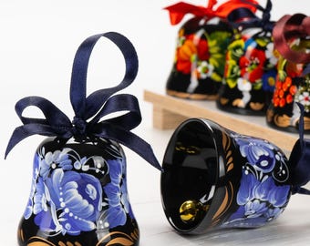 Puede incluir: Un conjunto de cinco campanas pintadas a mano con diseños florales. Las campanas son negras con detalles dorados y presentan flores azules, rojas y amarillas. Las campanas están atadas con cintas azules y rojas.