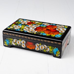 May include: A black wooden box with a hinged lid, decorated with hand-painted floral designs in red, orange, white, blue, and green. The box has a traditional Russian folk art style.