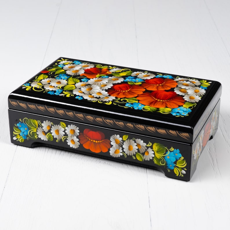 May include: A black wooden box with a hinged lid, decorated with hand-painted floral designs in red, orange, white, blue, and green. The box has a traditional Russian folk art style.