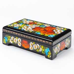 May include: A black wooden box with a hinged lid, decorated with hand-painted floral designs in shades of red, white, blue, and green. The box has a traditional Russian folk art style.