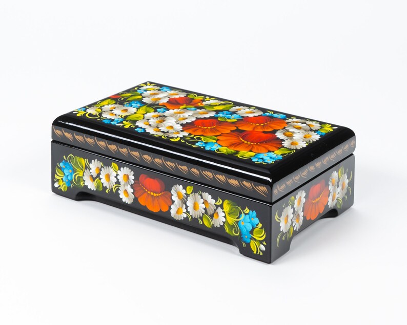 May include: A black wooden box with a hinged lid, decorated with hand-painted floral designs in shades of red, white, blue, and green. The box has a traditional Russian folk art style.