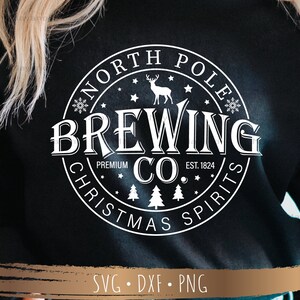 May include: Black sweatshirt with a white circular graphic that reads "NORTH POLE BREWING CO. CHRISTMAS SPIRITS EST. 1824." The design includes a reindeer, snowflakes, stars, and Christmas trees. The bottom of the image shows "SVG &bull; DXF &bull; PNG."