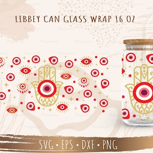 May include: A clear glass can with a gold and red hamsa hand and evil eye design. The can is 16 ounces and has a wooden lid. The design is on a white background. LIBBEY CAN GLASS WRAP 16 OZ is written in black text at the top of the image.