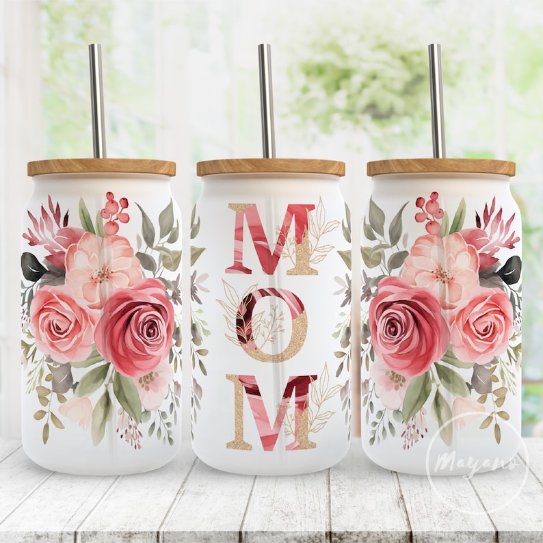 May include: Three white tumblers with lids and straws. The tumblers have a floral design with pink and red roses and green leaves. The middle tumbler has the word "MOM" in pink and gold letters.
