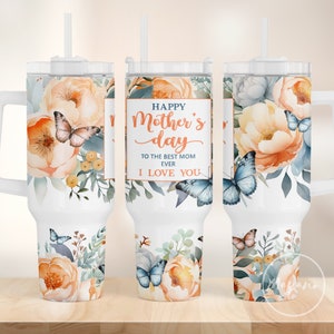 Puede incluir: Un vaso blanco con un diseño floral y mariposas. El vaso tiene un asa y una pajita. El texto en el vaso dice "Happy Mother's Day to the best mom ever I love you".