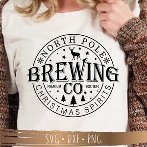 May include: White t-shirt featuring a black circular design with the text "NORTH POLE BREWING CO. CHRISTMAS SPIRITS". The design includes a deer, snowflakes, and pine trees. The shirt also has the text "EST. 1824".