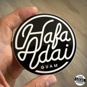 May include: A black and white sticker with the text "Hafa Adai GUAM" in a white cursive font.