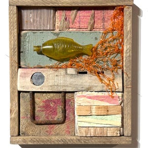 May include: A rectangular wooden wall hanging featuring a collage of weathered wood scraps, a translucent yellow fish-shaped bottle, a rusty metal U-shaped bracket, a circular metal insert, and a piece of orange plastic netting attached to the frame.