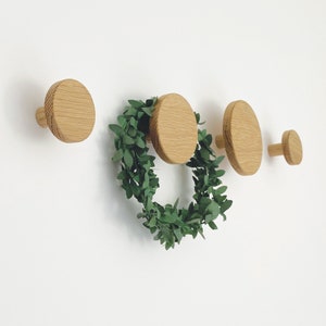 Op de afbeelding: Vier houten wandhaken in de vorm van cirkels, met een kleine groene krans die onder de middelste twee haken hangt.