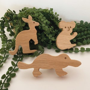 May include: Three wooden animal figurines: a kangaroo, a koala, and a platypus. The figurines are carved from light brown wood and have a simple, minimalist design.