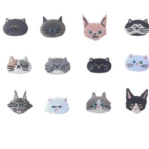 Op de afbeelding: Een verzameling geborduurde kattengezichtpatches in verschillende kleuren, waaronder zwart, grijs, roze en wit. Elke patch heeft gedetailleerde steken en verschillende gezichtsuitdrukkingen. De tekst "Longancraft" wordt boven de patches weergegeven.