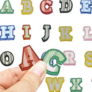 May include: Embroidered alphabet patches in various colours, including green, yellow, red, and blue. The patches feature a stitched border and are displayed against a white background. The brand name "Longancraft" is at the top.