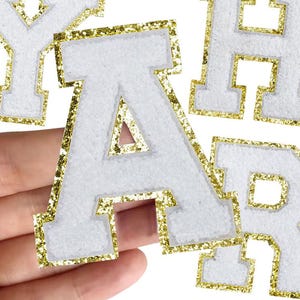 May include: White felt letter patches with gold glitter trim spelling out "YAHAR". The letters are held in a hand. The brand name "Longancraft" is at the top of the image.