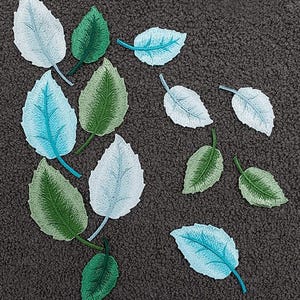 May include: Embroidered leaf patches in shades of green, blue, and white are scattered on a textured, dark gray surface. The patches vary in size and feature detailed stitching, with the brand name "Longancraft" at the top.