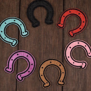 Peut inclure: Plusieurs patchs en forme de fer à cheval de couleurs variées : noir, rouge, rose, violet, turquoise et or. Chaque patch a une texture pailletée et un contour noir. Le texte "Longancraft" est affiché en haut.
