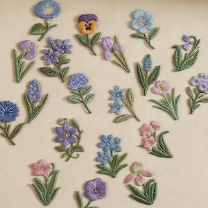 May include: Embroidered floral patches in various colors, including blue, purple, pink, and yellow, with green stems and leaves. The patches feature different flower types and the text "Longancraft".